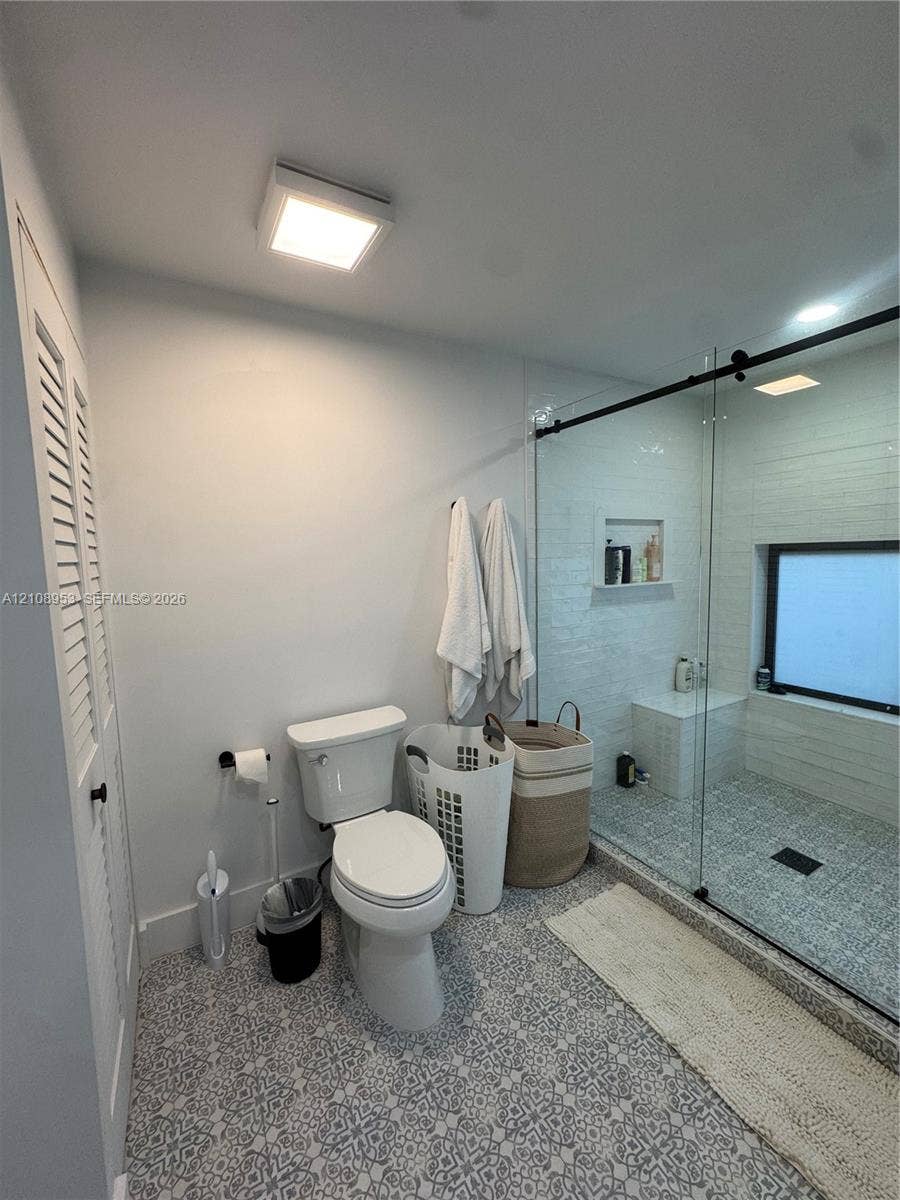 Walk-in shower featuring a frameless glass enclosure with matte black hardware, built-in shelving, a tiled bench, and patterned floor tile