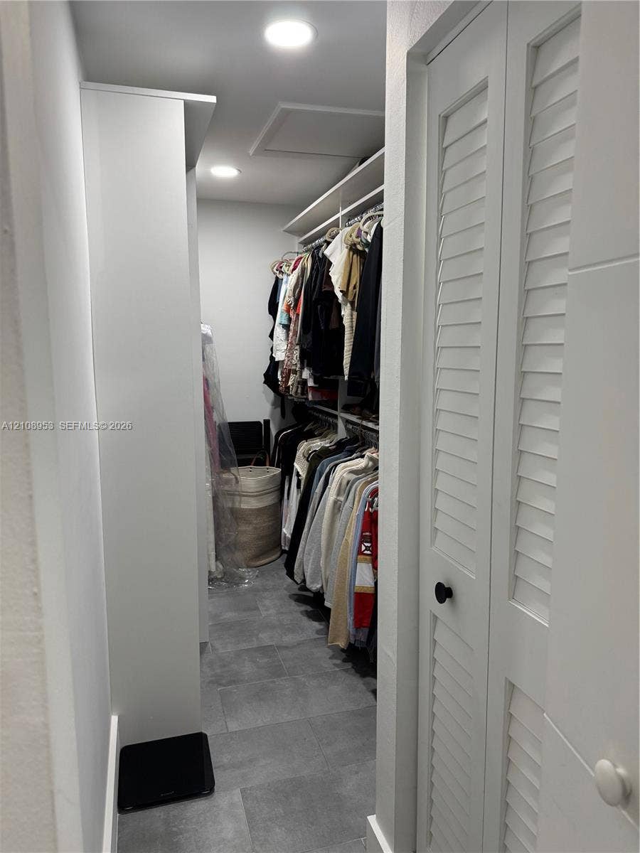 Walk-in storage space featuring ceramic tile flooring, built-in shelving, recessed lighting, and white louvered doors
