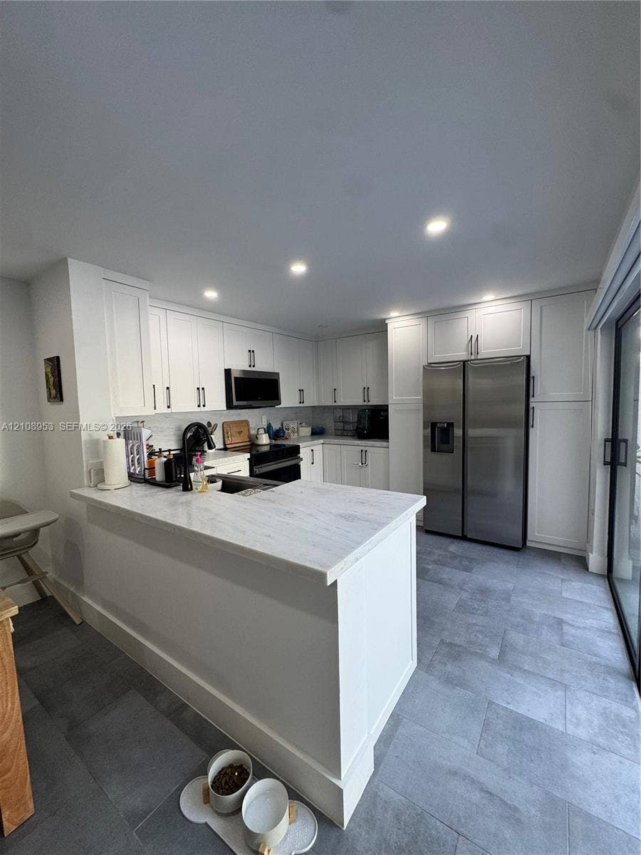 Kitchen featuring white shaker-style cabinetry, stone-finish countertops, stainless steel side-by-side refrigerator, recessed ceiling lighting, and large-format tile flooring