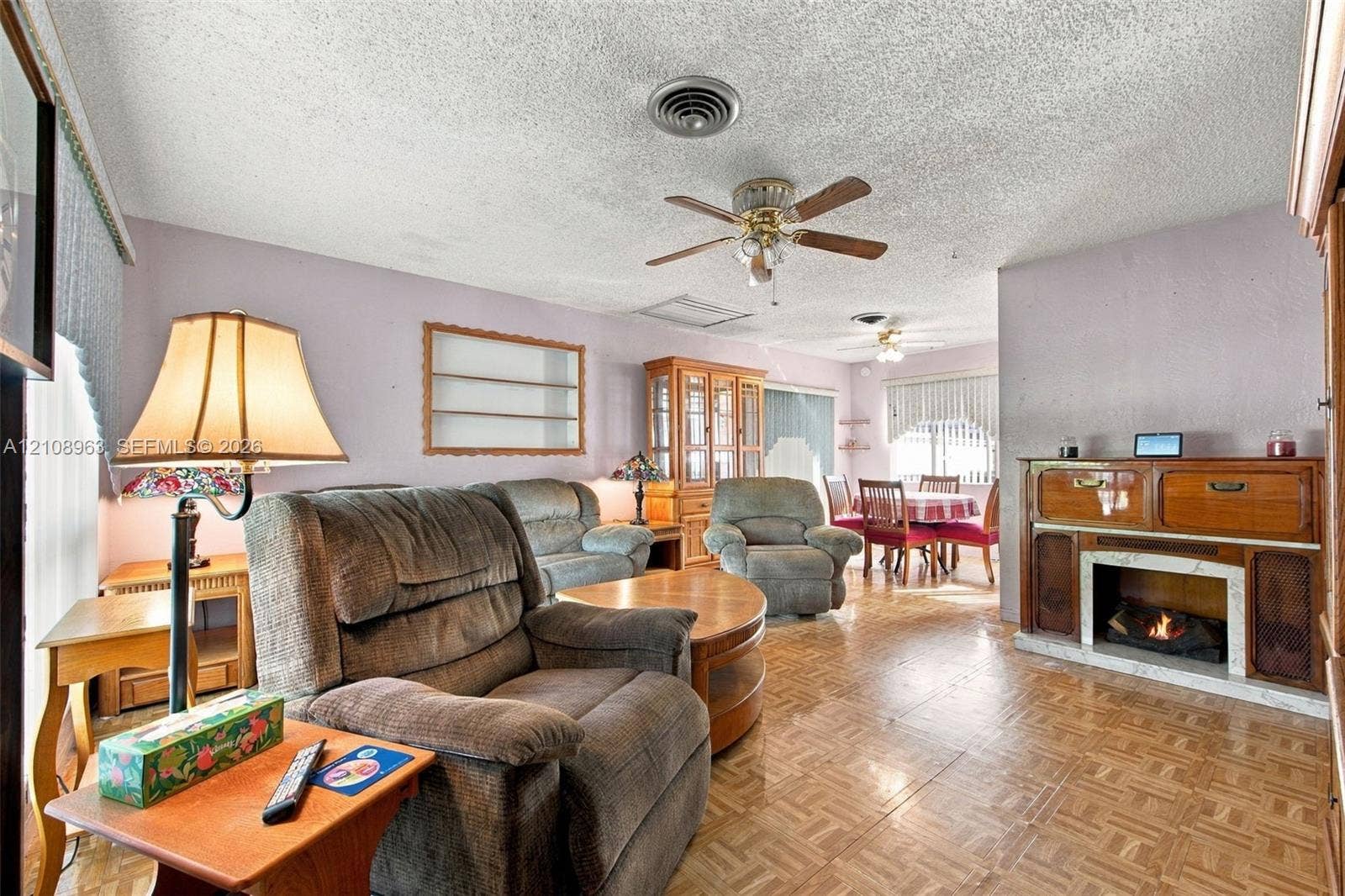 Living area featuring wood-finish parquet flooring, fireplace with stone surround, wall-mounted display shelving, ceiling-mounted paddle fans, and built-in cabinetry