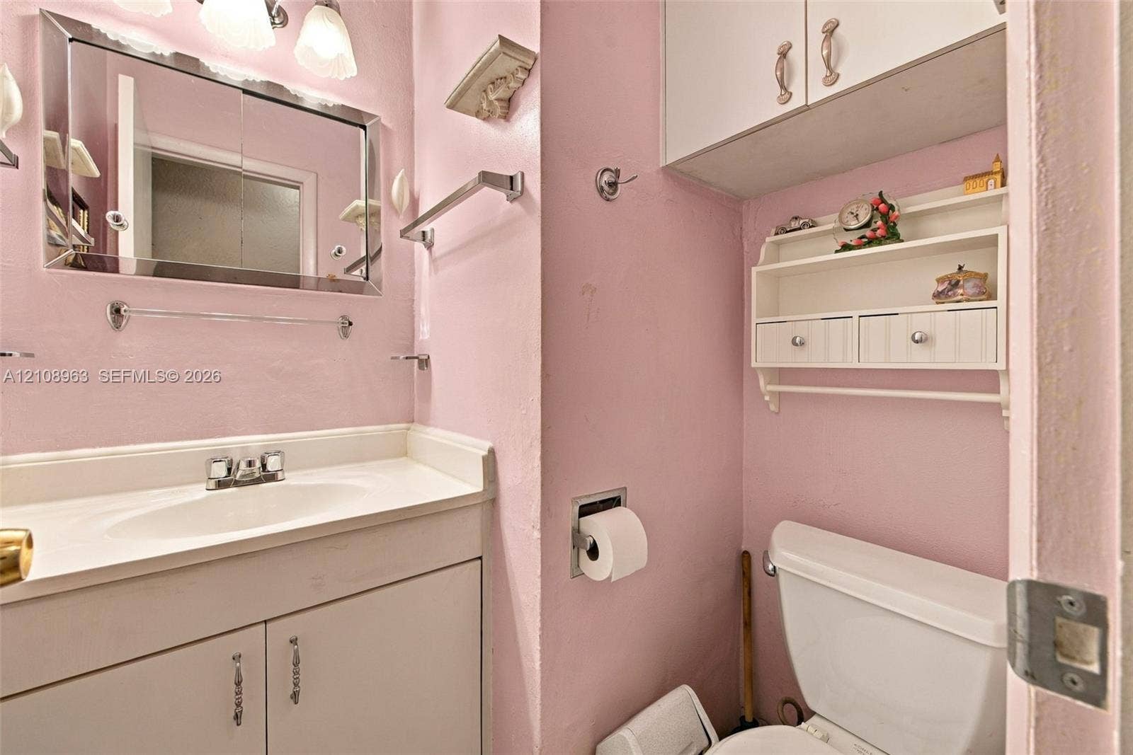 Bathroom featuring a vanity with integrated sink, rectangular framed mirror, upper cabinetry, and mounted storage shelving