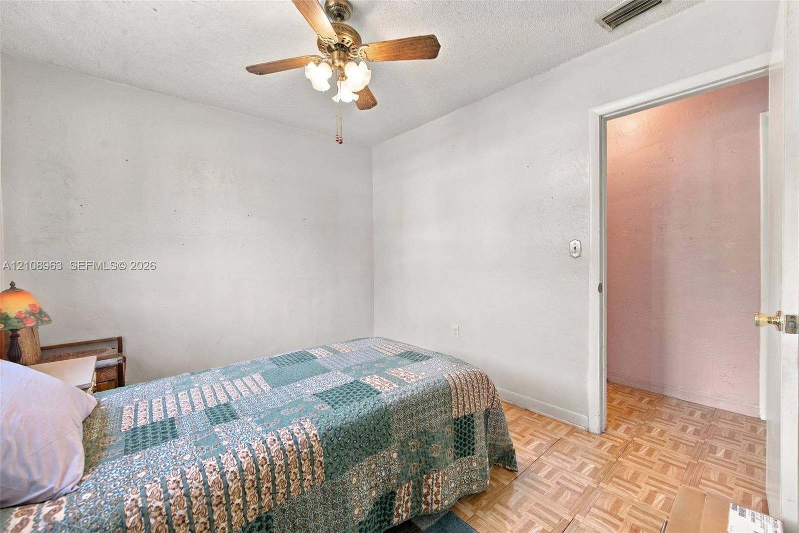 Room featuring parquet wood-finish flooring, a ceiling fan with multi-bulb light fixture, and an entry to a walk-in space