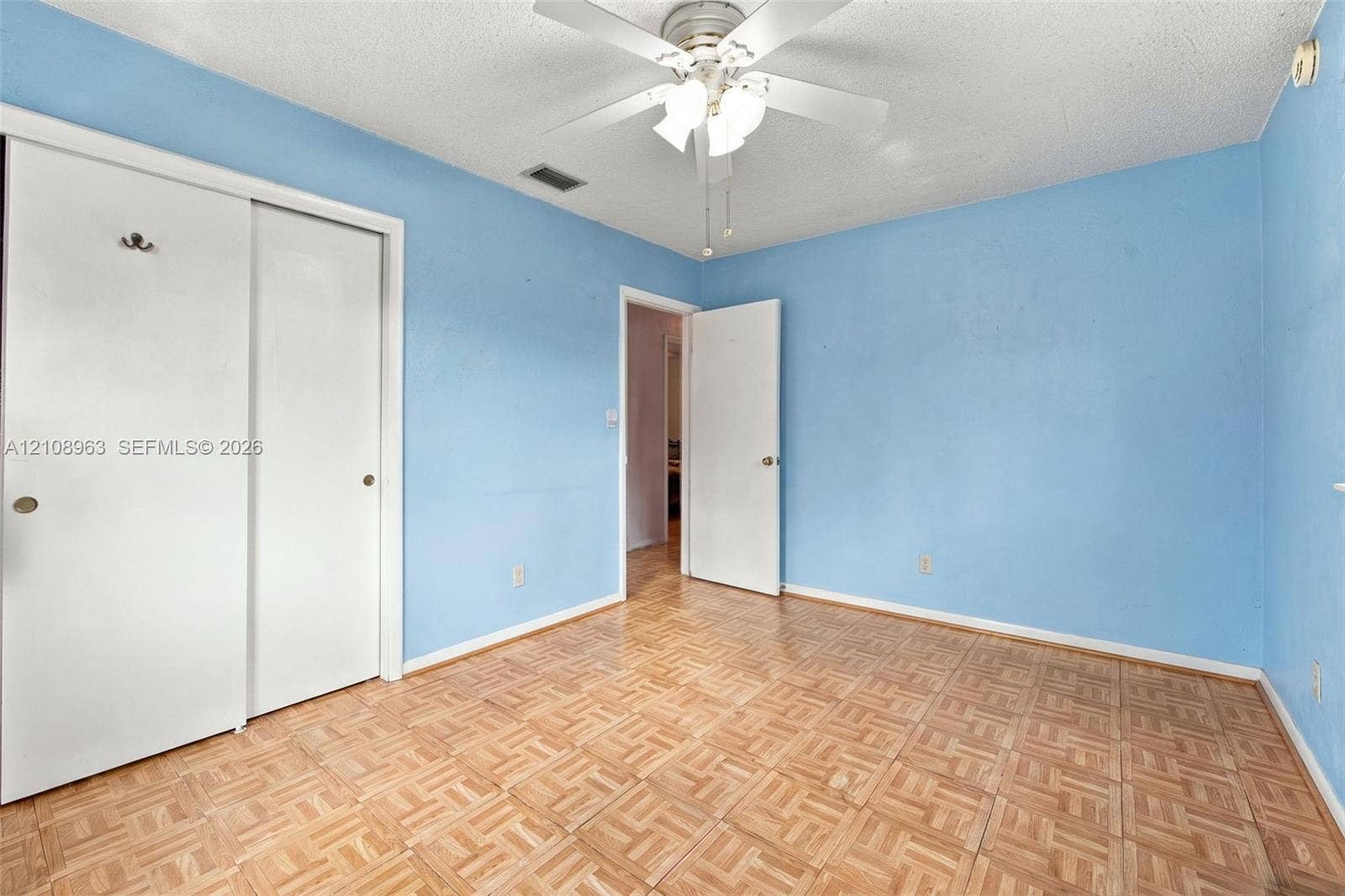 Parquet wood-finish flooring, sliding closet doors, and ceiling-mounted light fixture with a fan