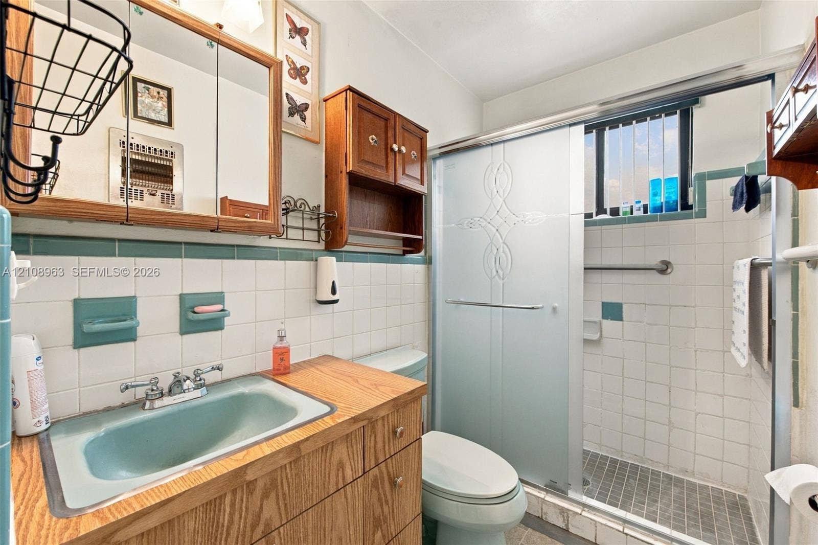 Bathroom featuring a wood vanity with a dual-handle faucet, integrated medicine cabinet, shower enclosure with glass sliding doors, and tiled wall accents