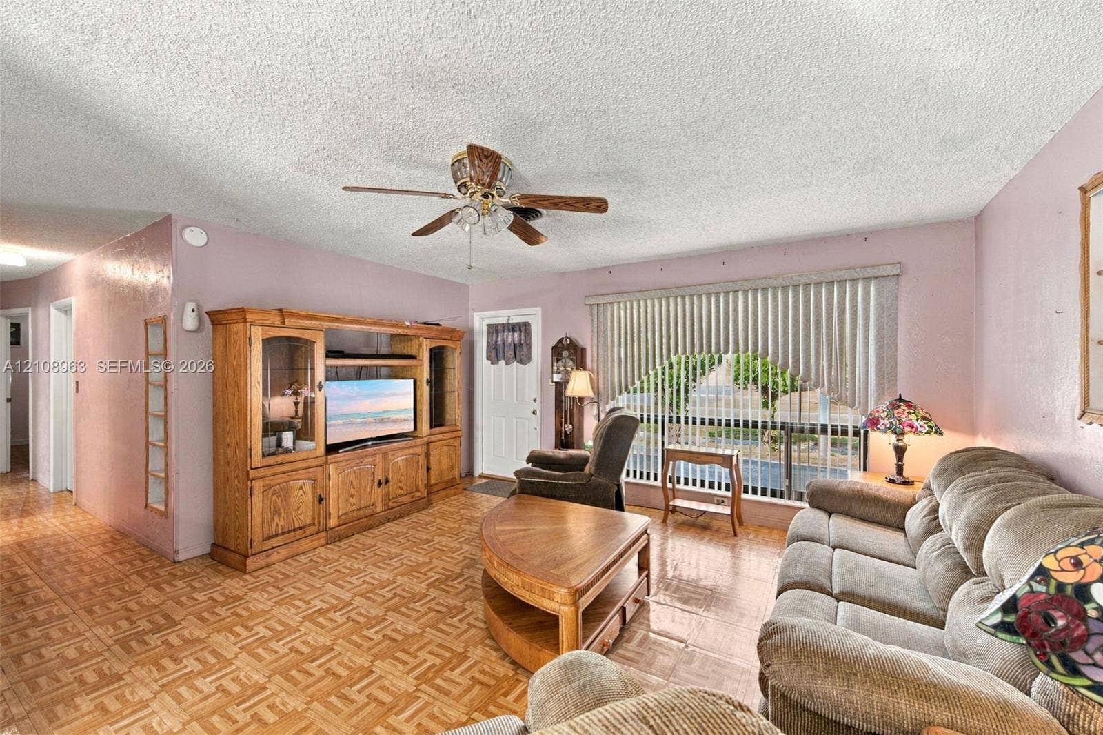 Living area featuring parquet flooring, built-in wooden cabinetry, a ceiling fan with integrated lighting, and vertical window blinds