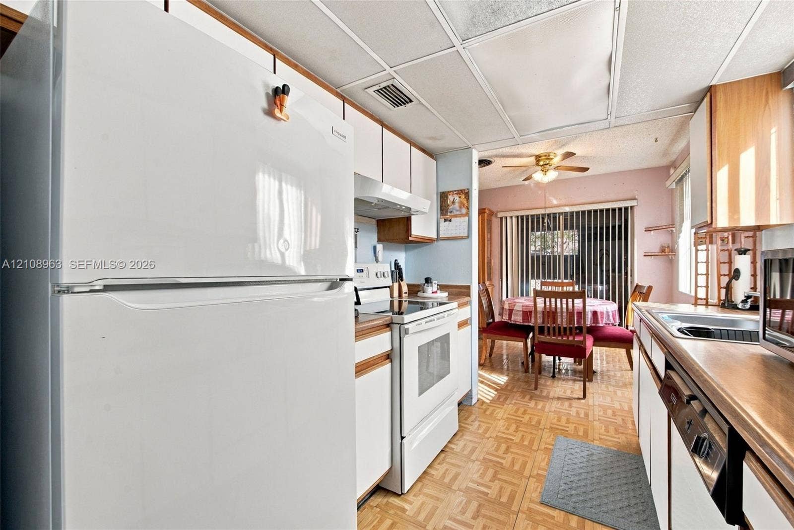 Kitchen featuring white cabinetry, light-toned laminate countertops, integrated white appliances, and parquet-style flooring