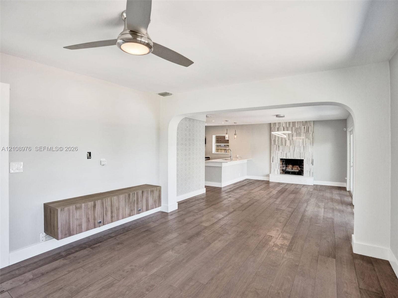 525 SW 12th Street, Fort Lauderdale, Fort Lauderdale, FL 33315 Wood-finish flooring, brushed-nickel ceiling fan with integrated lighting, wall-mounted wood-finish cabinetry, arched entryway, and fireplace with vertical tile surround