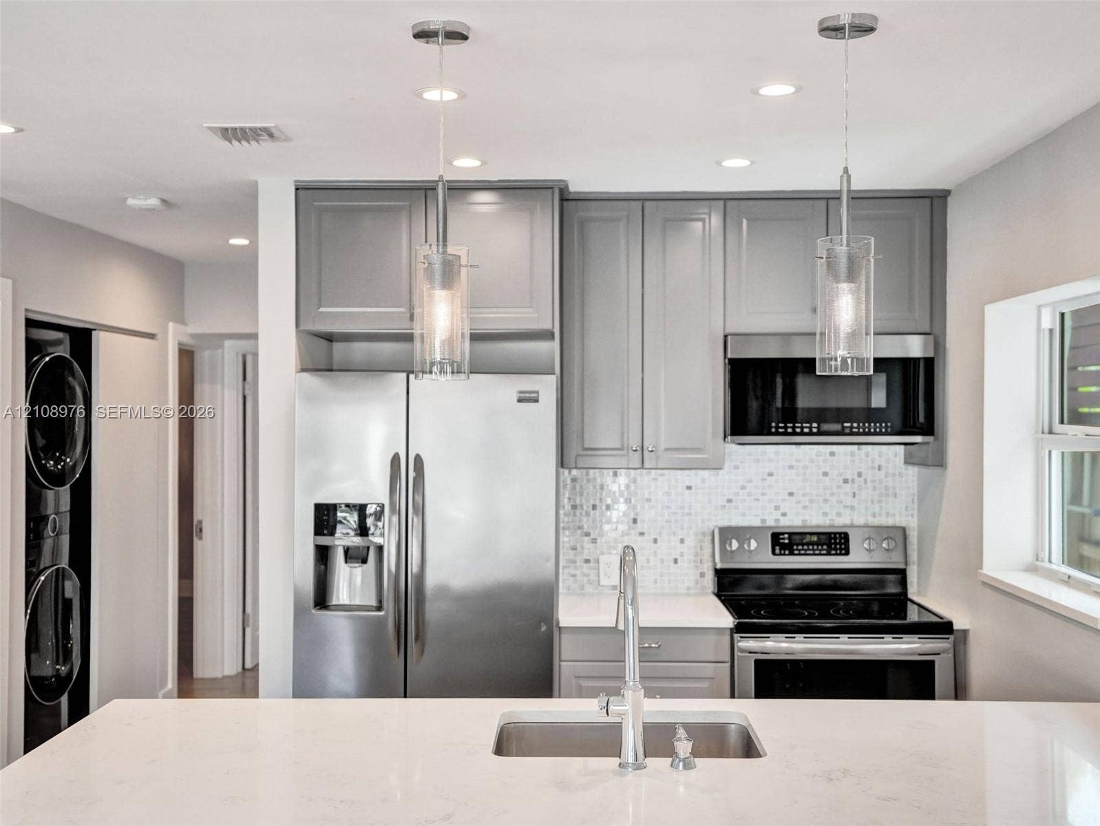 525 SW 12th Street, Fort Lauderdale, Fort Lauderdale, FL 33315 Kitchen featuring grey shaker-style cabinetry, stainless steel appliances, white stone-finish countertops, a mosaic tile backsplash, and dual glass pendant lights