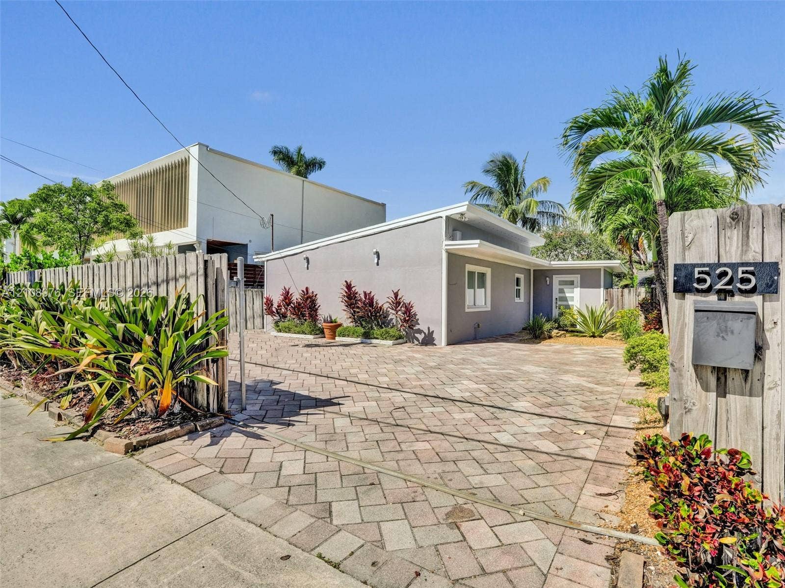 525 SW 12th Street, Fort Lauderdale, Fort Lauderdale, FL 33315 Single-story residence featuring a paved brick driveway, low-slope roofline, light-toned exterior finish, and fenced perimeter