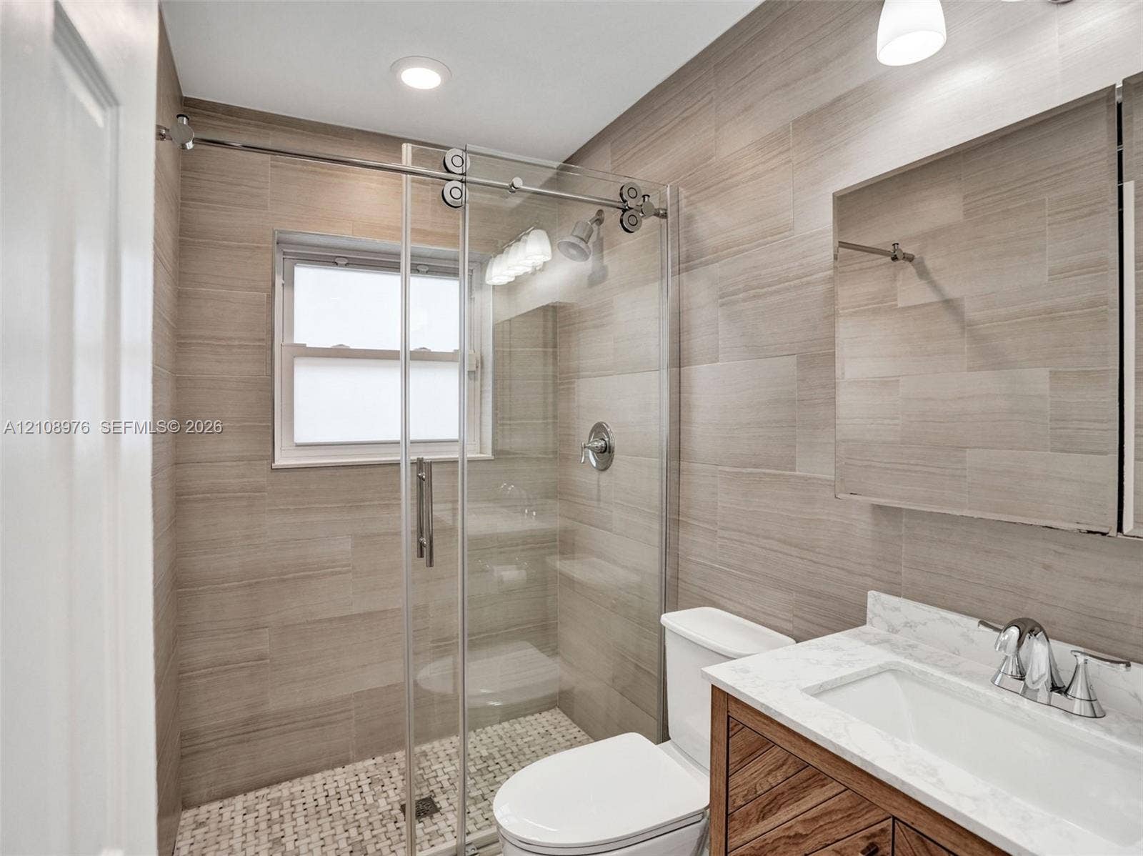 525 SW 12th Street, Fort Lauderdale, Fort Lauderdale, FL 33315 Walk-in shower with sliding glass door, mosaic floor tiling, full-height wall tile, wood-finish vanity with stone countertop, and recessed ceiling lighting