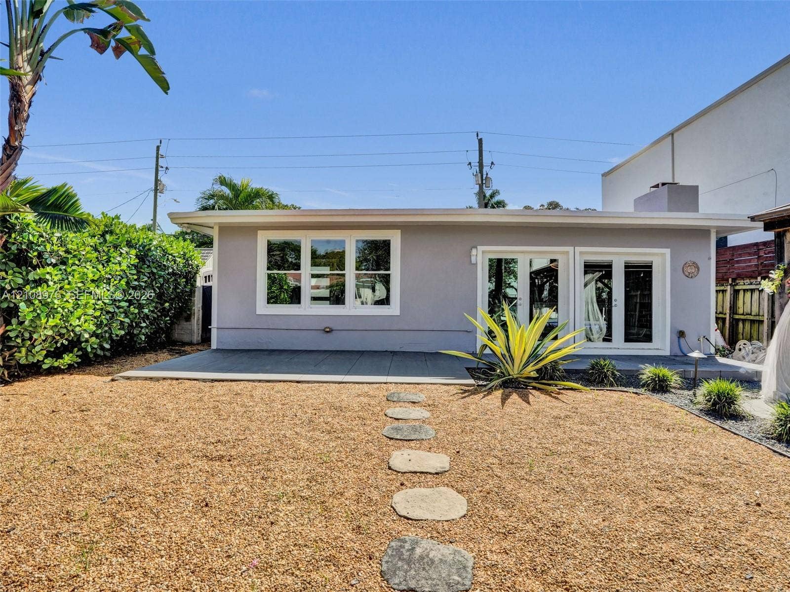 525 SW 12th Street, Fort Lauderdale, Fort Lauderdale, FL 33315 Rear exterior featuring a concrete patio, dual glass-paneled double doors, horizontal multi-pane windows, and a stone-paver walkway set within a gravel yard