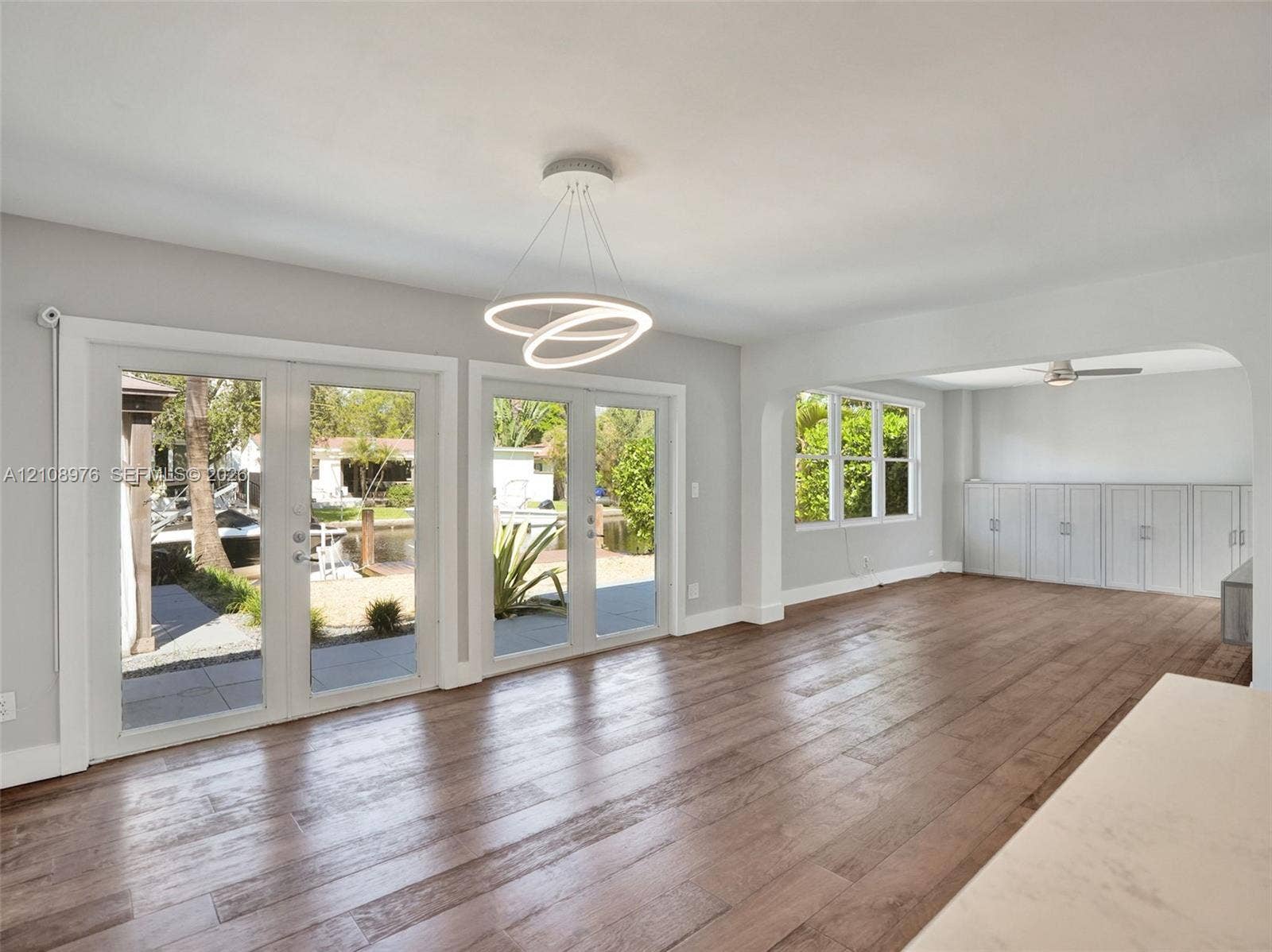 525 SW 12th Street, Fort Lauderdale, Fort Lauderdale, FL 33315 Living space featuring wood-finish flooring, dual sets of French doors, an integrated circular LED light fixture, and custom built-in cabinetry with an arched room partition