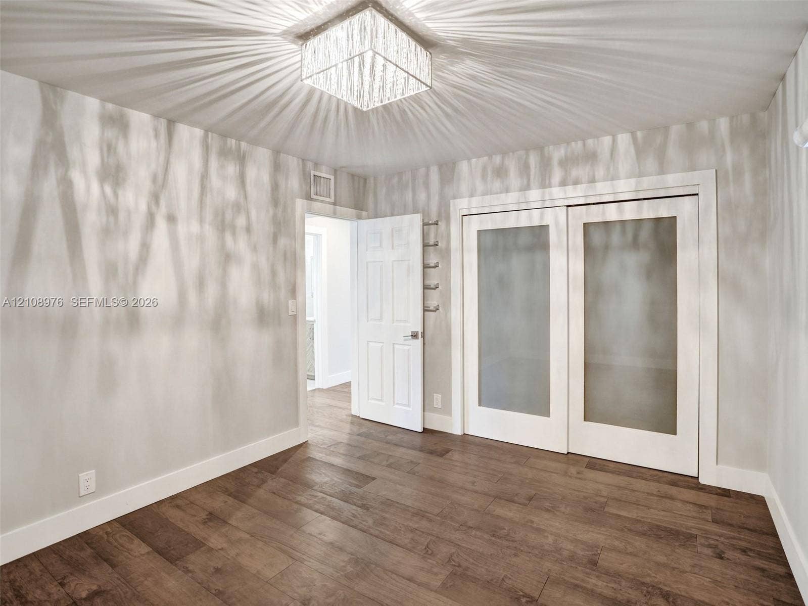 525 SW 12th Street, Fort Lauderdale, Fort Lauderdale, FL 33315 Wood-finish flooring featuring a square, multi-faceted crystal ceiling fixture, dual-panel sliding doors with frosted glass inserts, and a six-panel interior door