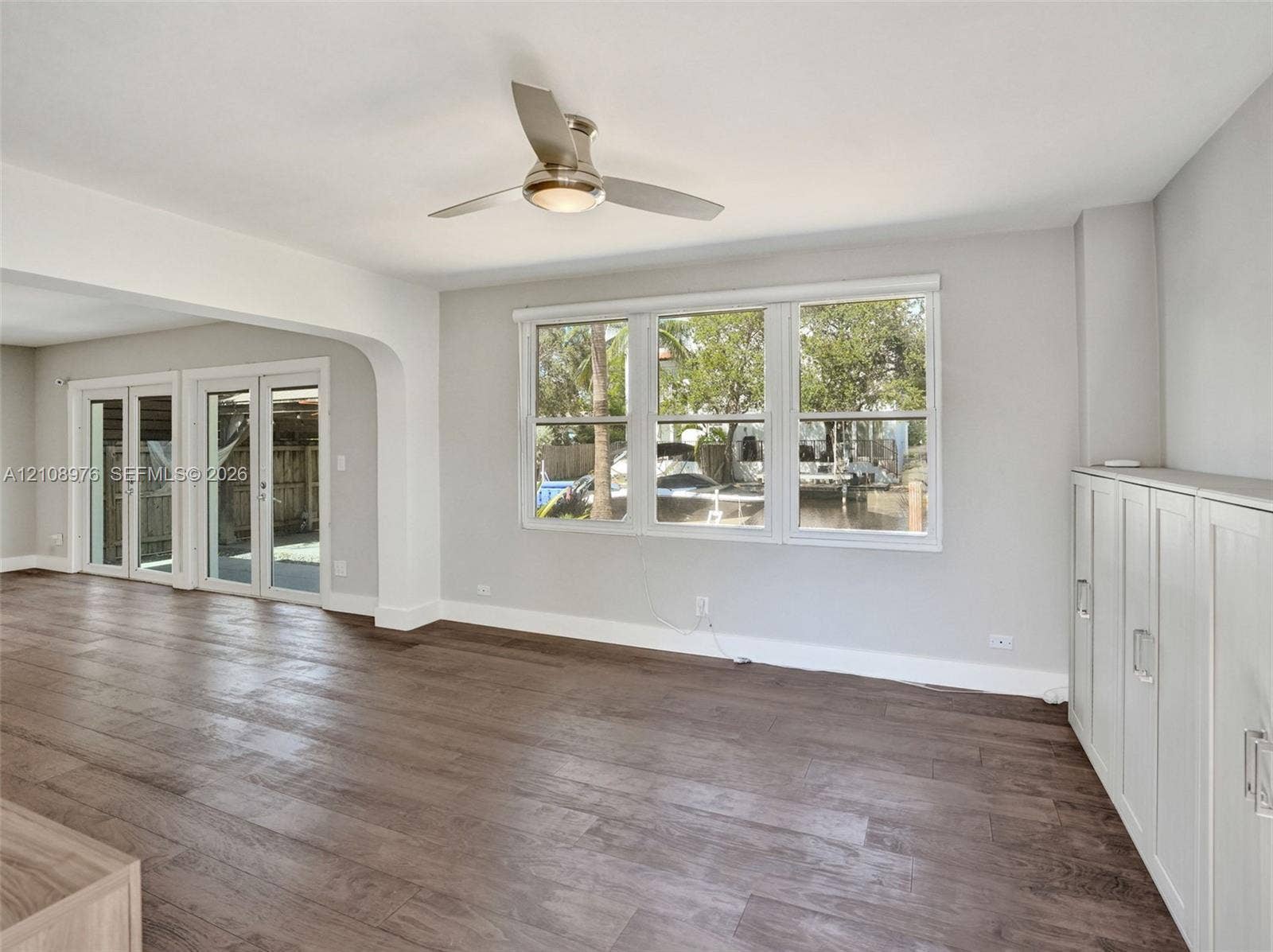 525 SW 12th Street, Fort Lauderdale, Fort Lauderdale, FL 33315 Open living area featuring wood-finish flooring, a contemporary ceiling fan with integrated lighting, triple-pane window configuration, and built-in white cabinetry