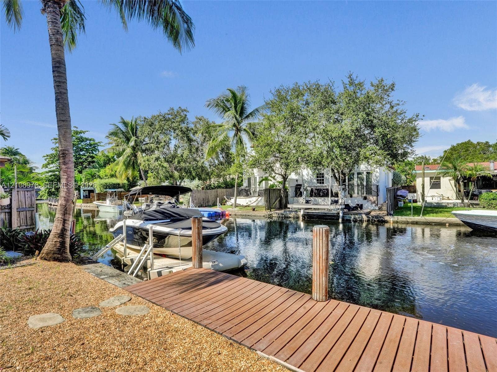 525 SW 12th Street, Fort Lauderdale, Fort Lauderdale, FL 33315 Waterfront canal property featuring a private wood-plank dock, boat lift, gravel landscaping, and mature palm trees