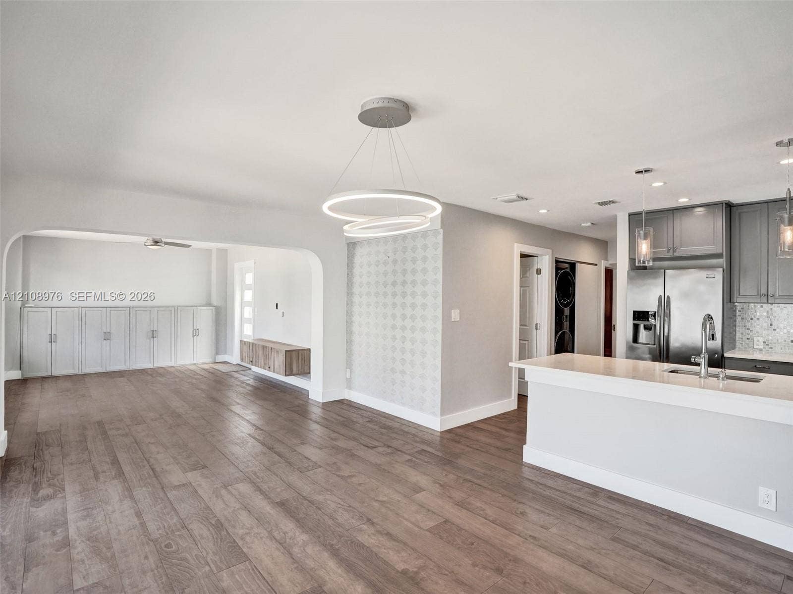 525 SW 12th Street, Fort Lauderdale, Fort Lauderdale, FL 33315 Open-concept interior featuring wood-finish flooring, a modern dual-ring pendant light fixture, cabinetry with stone countertops, and a decorative tile accent wall