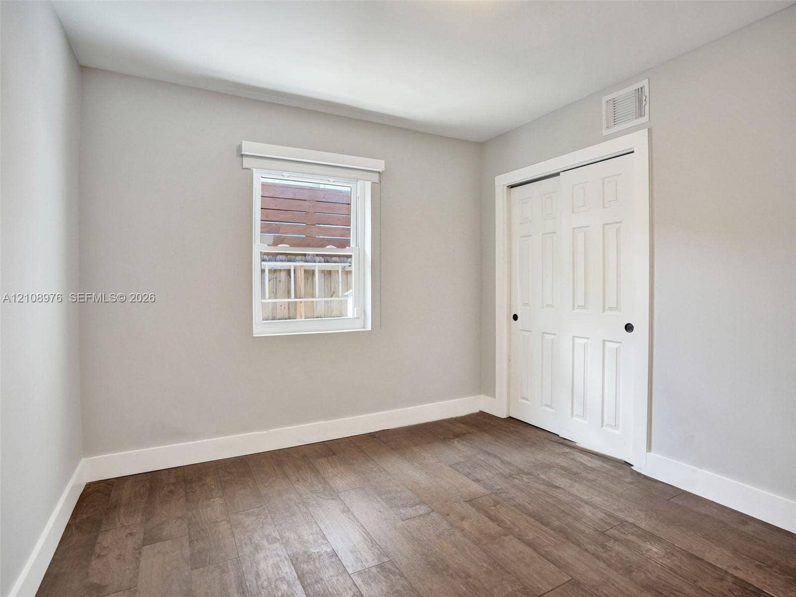 525 SW 12th Street, Fort Lauderdale, Fort Lauderdale, FL 33315 Bedroom 2. Neutral interior featuring wood-finish flooring, white paneled sliding closet doors, and a single-hung window with a classic valance