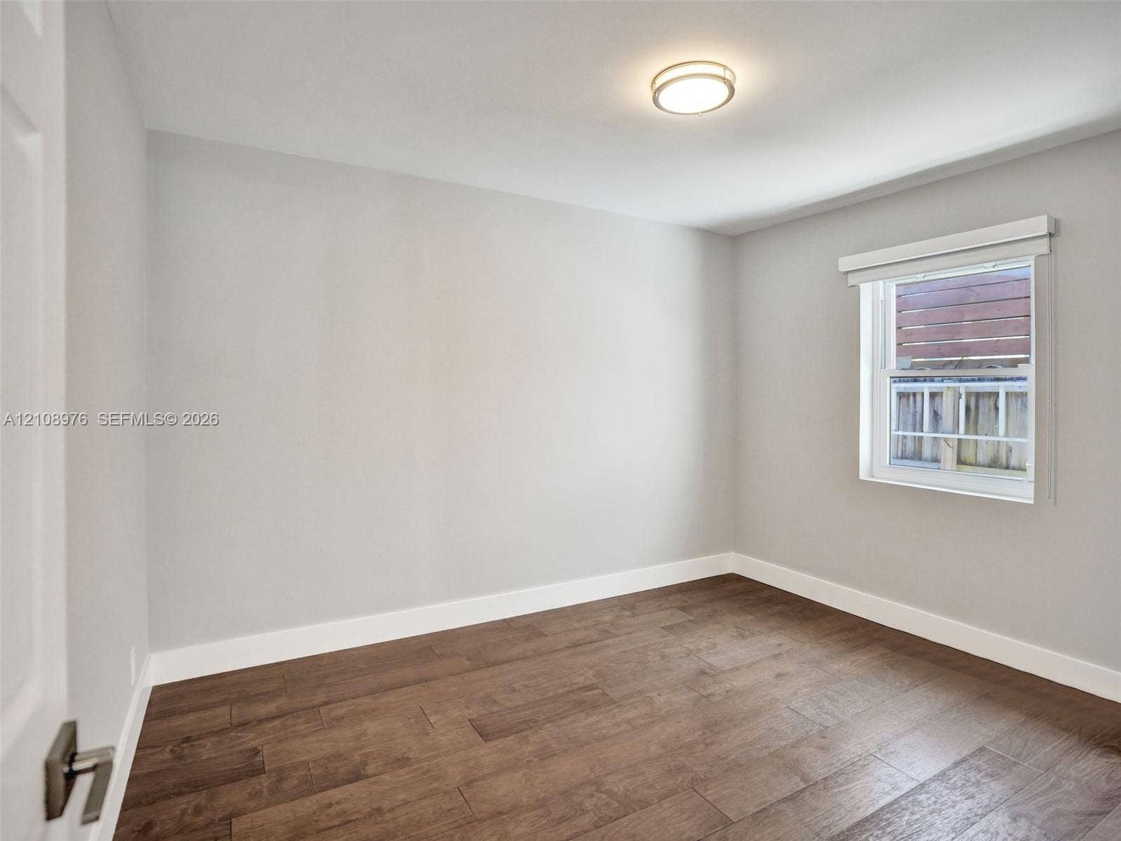 525 SW 12th Street, Fort Lauderdale, Fort Lauderdale, FL 33315 Bedroom 2. Interior space featuring neutral wall paint, wood-finish flooring, a flush-mount ceiling light fixture, and a single-hung window with a roller shade