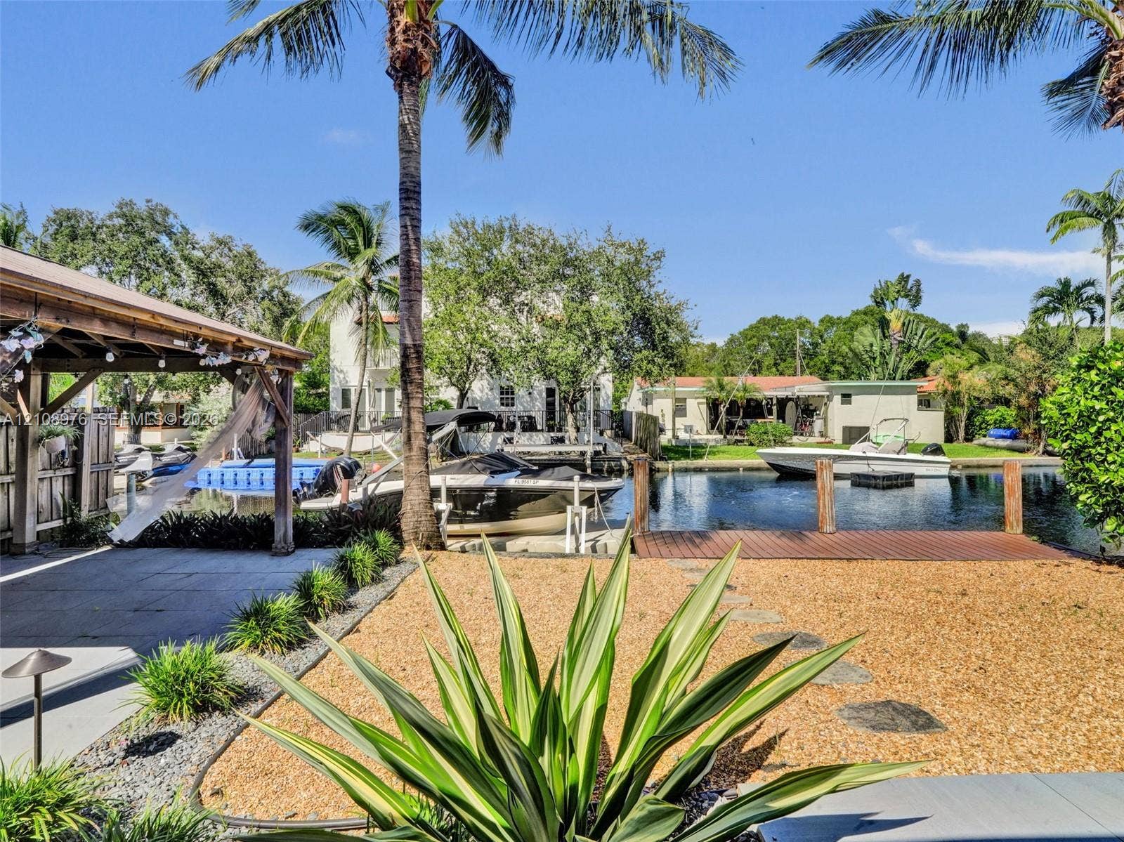 525 SW 12th Street, Fort Lauderdale, Fort Lauderdale, FL 33315 Waterfront property featuring a covered pergola, private wood-plank dock, gravel landscaping, and mature palm trees