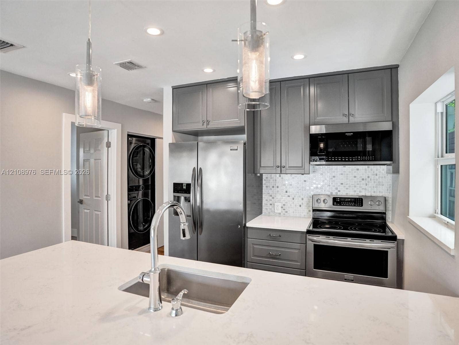 525 SW 12th Street, Fort Lauderdale, Fort Lauderdale, FL 33315 Kitchen featuring grey shaker-style cabinetry, white stone-finish countertops, stainless steel appliances, mosaic tile backsplash, and glass pendant lighting