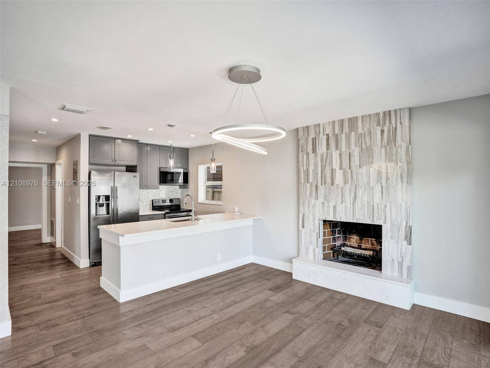 525 SW 12th Street, Fort Lauderdale, Fort Lauderdale, FL 33315 Open concept interior featuring wood-finish flooring, a kitchen with quartz countertops and stainless steel appliances, and a floor-to-ceiling textured stone fireplace surround
