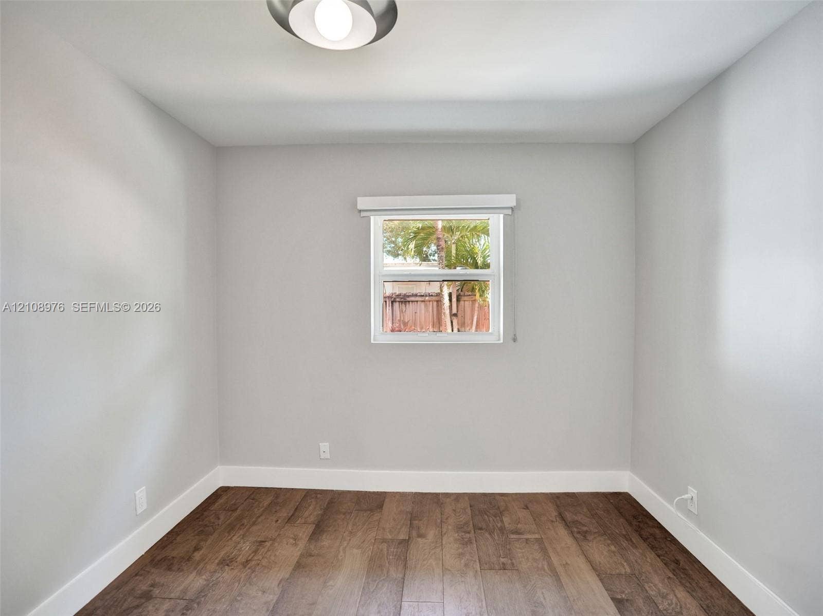 525 SW 12th Street, Fort Lauderdale, Fort Lauderdale, FL 33315 Bedroom 3. Neutral wall paint, wood-finish flooring, and single-pane window with installed window treatment, complemented by a flush-mount ceiling fixture