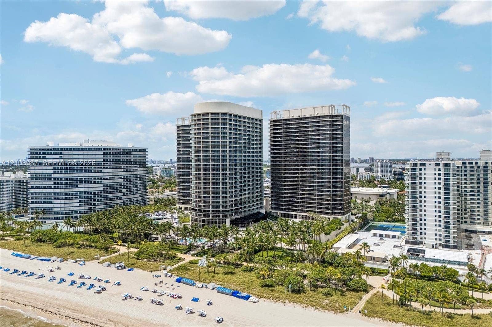 High-rise residential towers featuring expansive balconies, tropical landscaping, and direct access to a sandy coastline