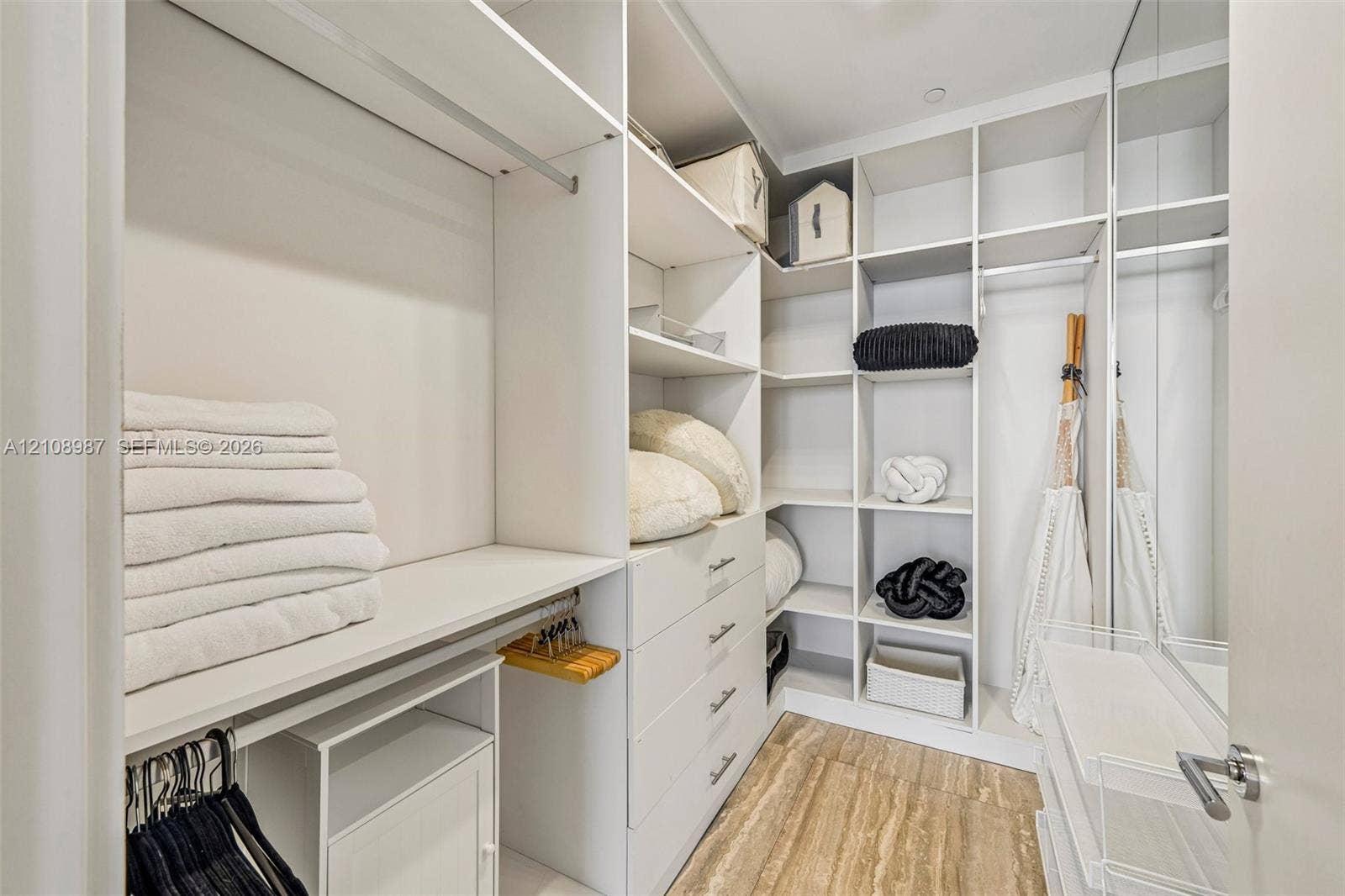 Walk-in closet featuring white custom built-in cabinetry, floor-to-ceiling shelving, integrated storage drawers with metal hardware, and wood-finish flooring