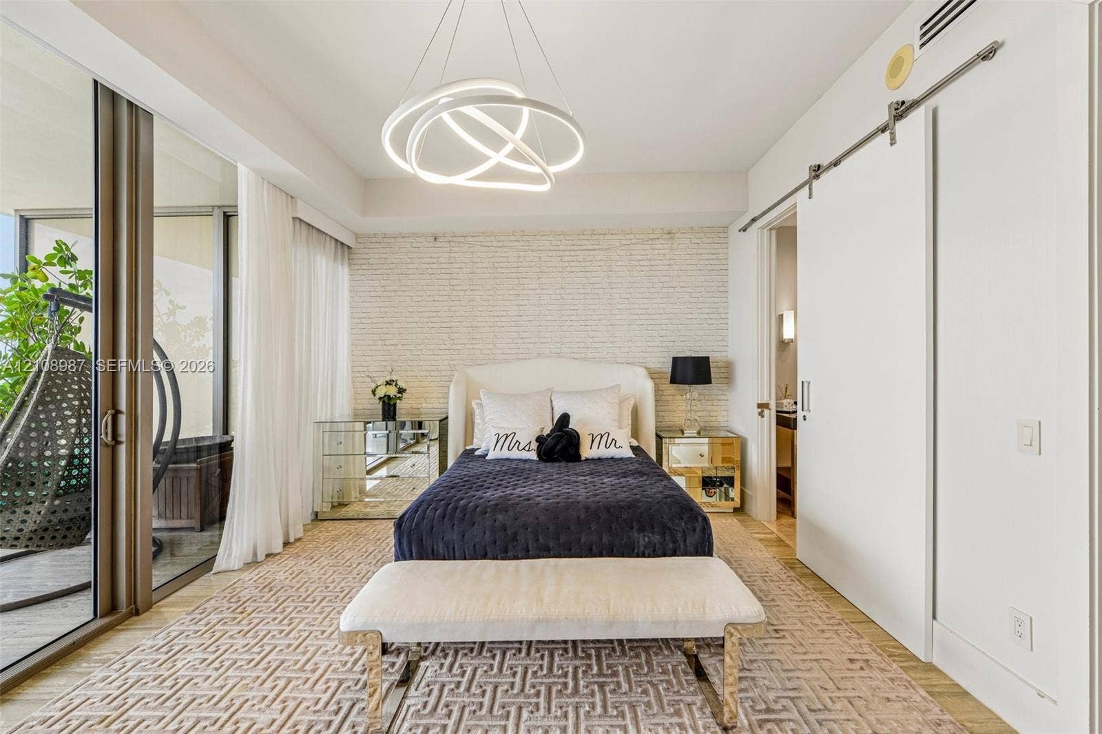 Textured brick accent wall, sculptural circular LED chandelier, floor-to-ceiling glass sliding doors, and white sliding barn door