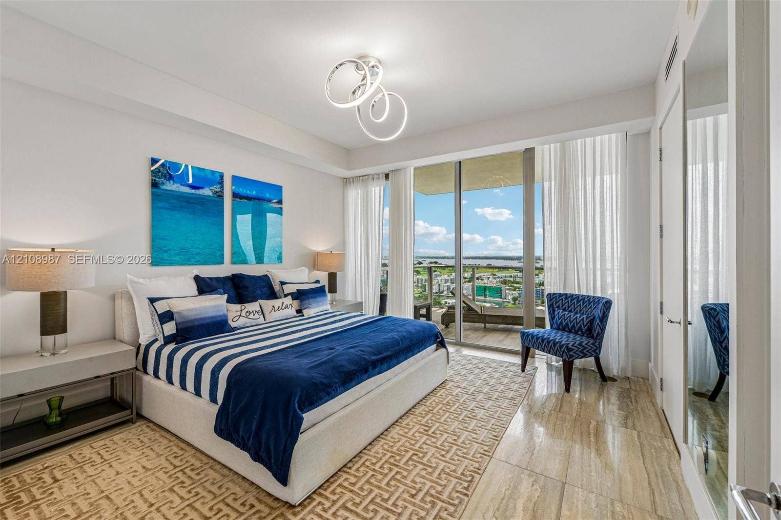 Floor-to-ceiling sliding glass doors, natural stone flooring, modern geometric LED chandelier, and a private balcony