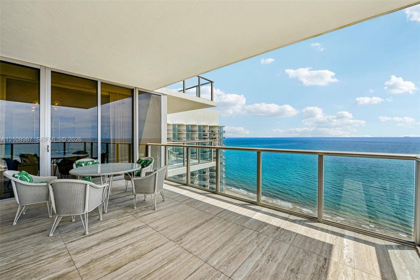 Covered balcony featuring large-format stone-finish tile flooring, floor-to-ceiling glass sliding doors, and a metal railing with a glass panel insert