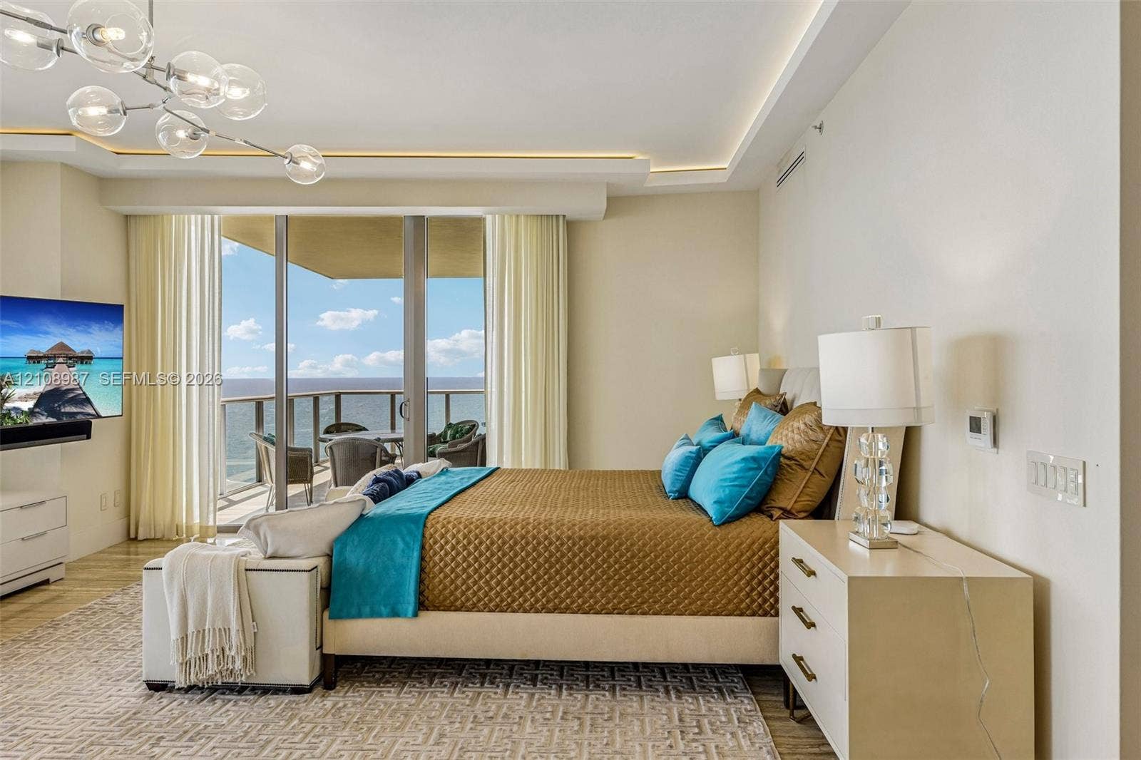 Tray ceiling with recessed lighting, multi-globe chandelier, floor-to-ceiling glass door, and balcony with metal railing