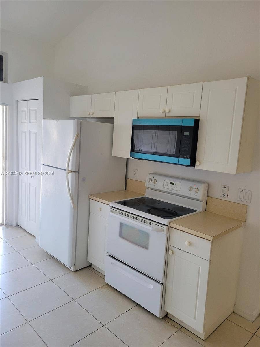 Kitchen featuring white cabinetry, light-toned countertops, a full-sized white refrigerator, a white electric range, an over-the-range microwave, and ceramic tile flooring