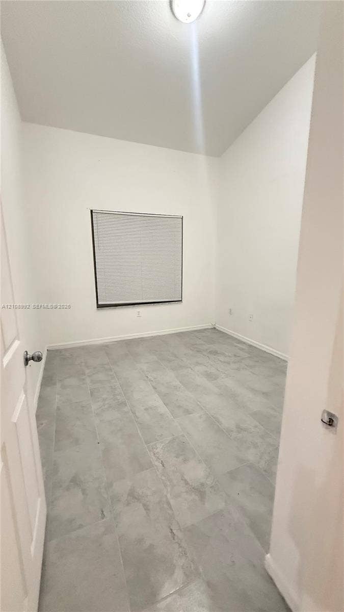 Interior space featuring high vaulted ceilings, large-format grey tile flooring, and a single window with fitted blinds