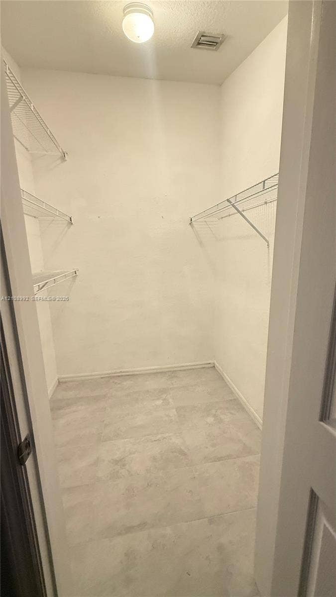 Walk-in closet featuring light-toned tile flooring, multi-level wire shelving, and a ceiling-mounted light fixture