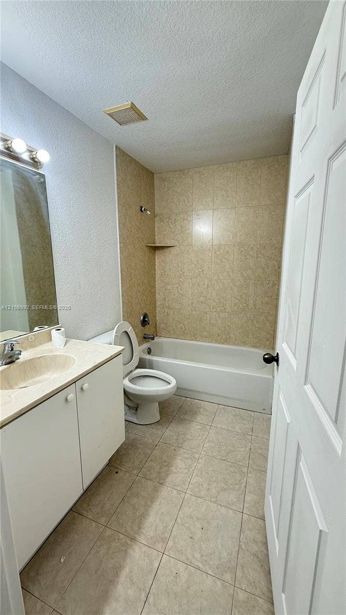 Bathroom featuring a white vanity cabinet with an integrated sink, ceramic tile flooring, a tub-shower combination with tiled surround, and wall-mounted vanity lighting