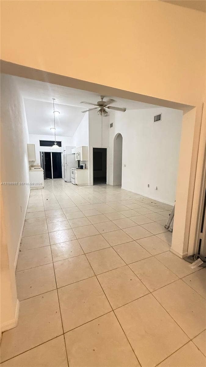 Open-concept interior featuring vaulted ceilings, light-colored tile flooring, a built-in kitchen, and arched architectural detailing