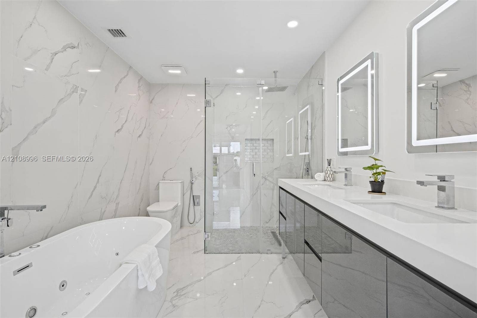 4252 SW 131st Avenue, Miami, FL 33175 Full-wall veined stone-look tiling, jetted soaking tub, dual-sink vanity with high-gloss cabinetry, glass-enclosed walk-in shower with stone tile flooring, and integrated LED-lighted mirrors