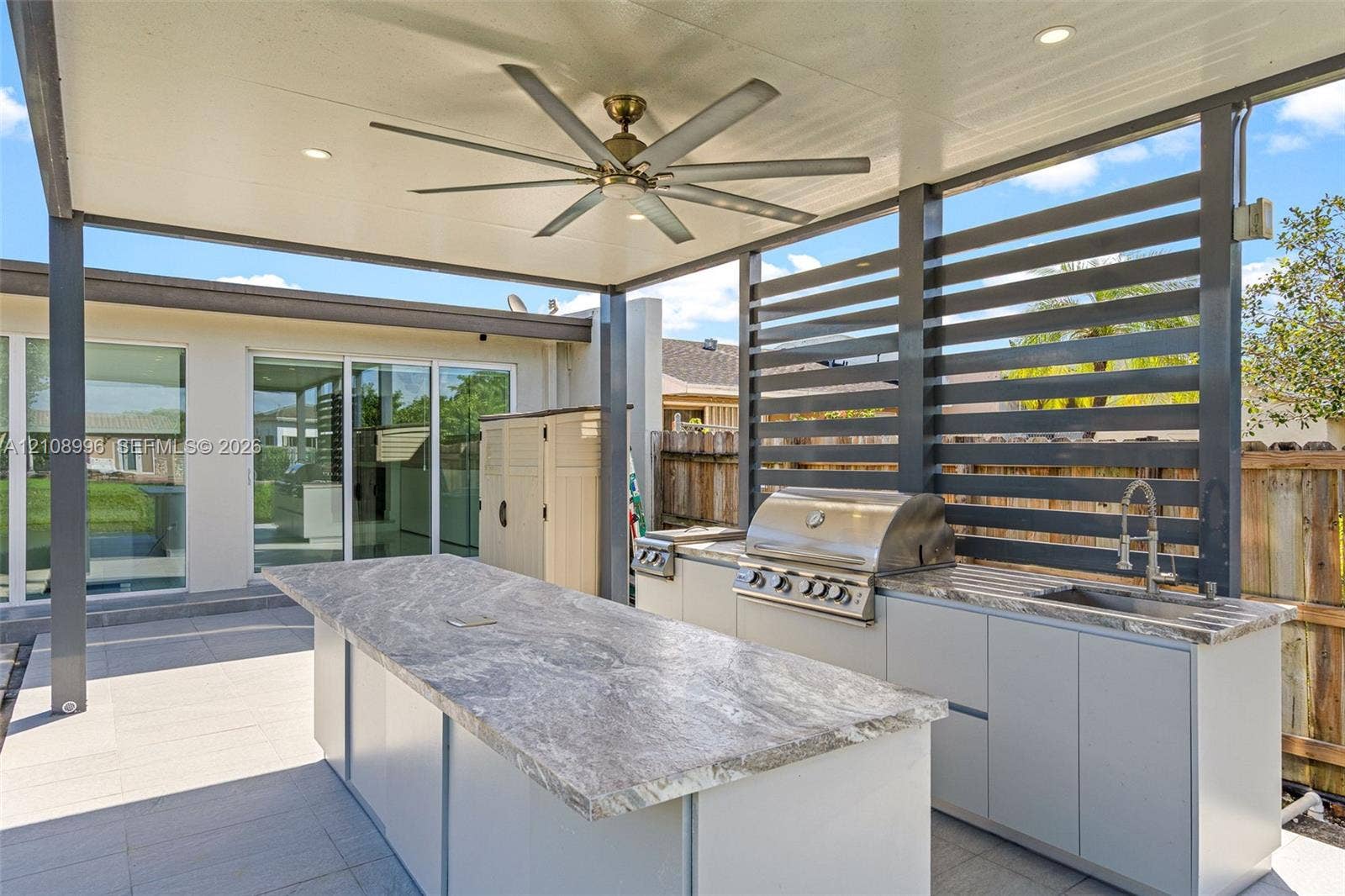 4252 SW 131st Avenue, Miami, FL 33175 Covered outdoor kitchen featuring stone-top counters, a stainless steel built-in grill, a sink, and a multi-blade ceiling fan under a structured patio roof