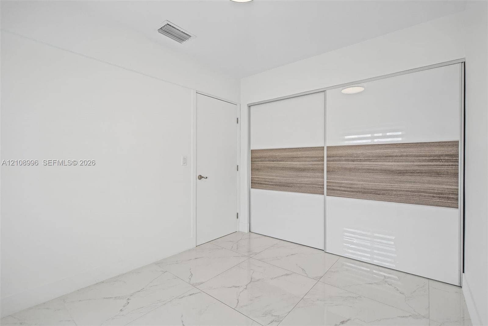 4252 SW 131st Avenue, Miami, FL 33175 Large-format polished tile flooring featuring a veined pattern, dual sliding closet doors with high-gloss white and wood-finish detailing, and a solid-core interior door