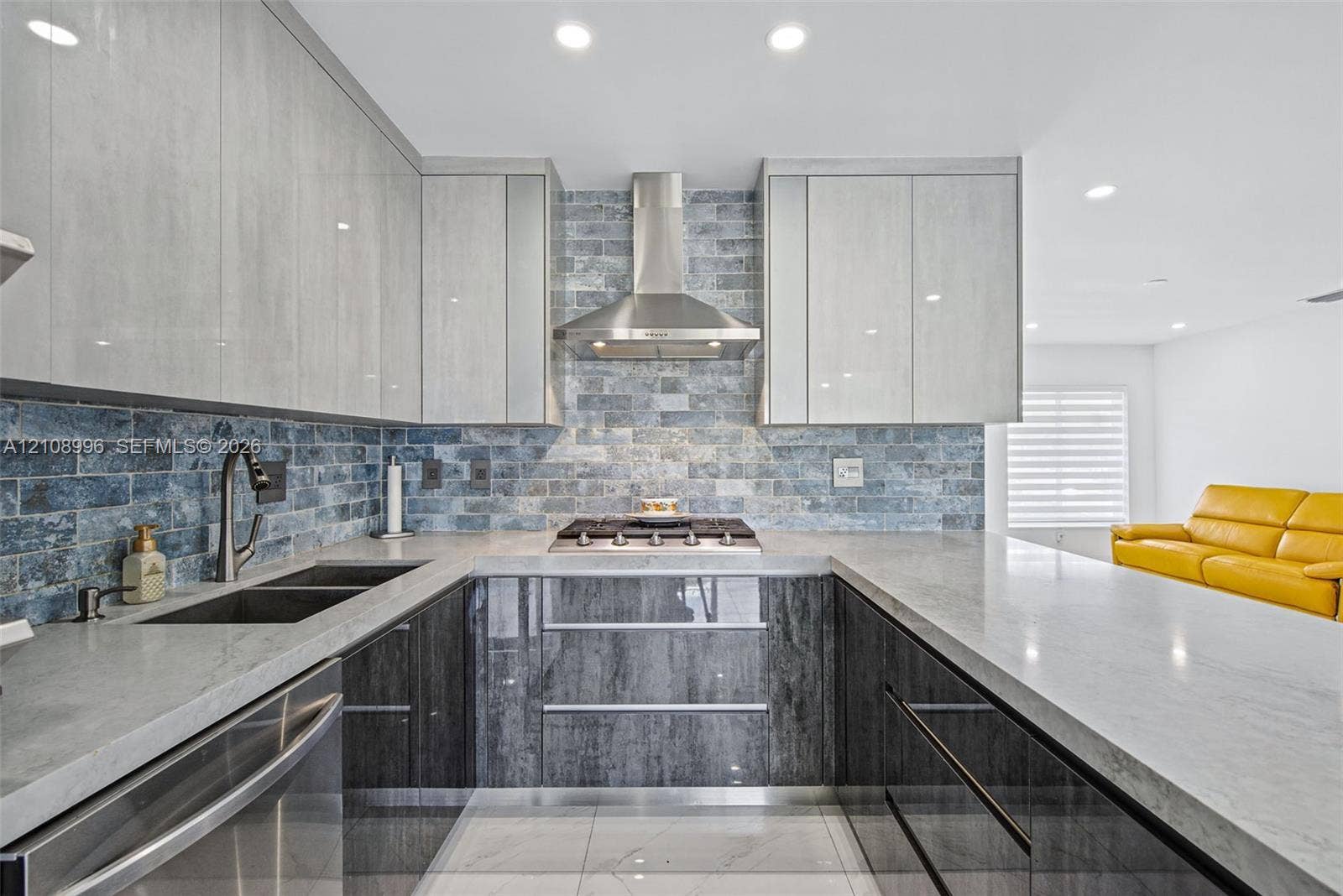 4252 SW 131st Avenue, Miami, FL 33175 Kitchen featuring two-tone flat-panel cabinetry, stone-finish countertops, brick-style tile backsplash, stainless steel gas cooktop with chimney-style range hood, and integrated stainless steel sink with pull-down faucet
