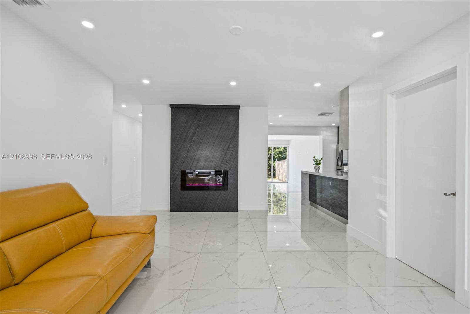 4252 SW 131st Avenue, Miami, FL 33175 Full-height dark stone fireplace feature, recessed LED lighting, white large-format tile flooring, and sleek built-in kitchen cabinetry