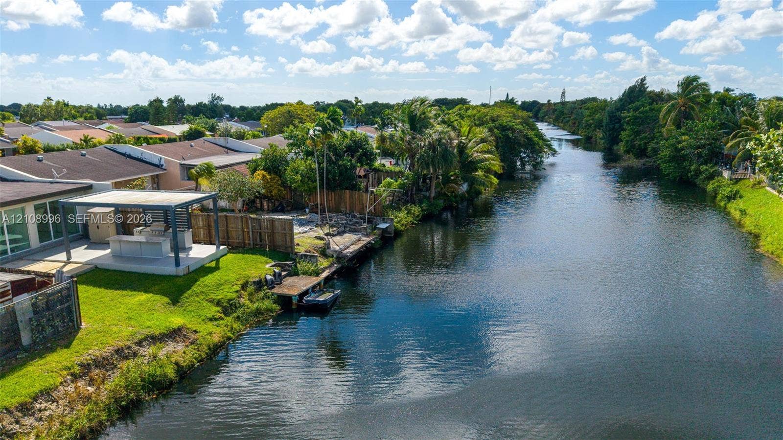 4252 SW 131st Avenue, Miami, FL 33175 Waterfront property featuring a canal-side bulkhead, a private boat dock, and a covered outdoor kitchen structure situated on a grass-covered lot