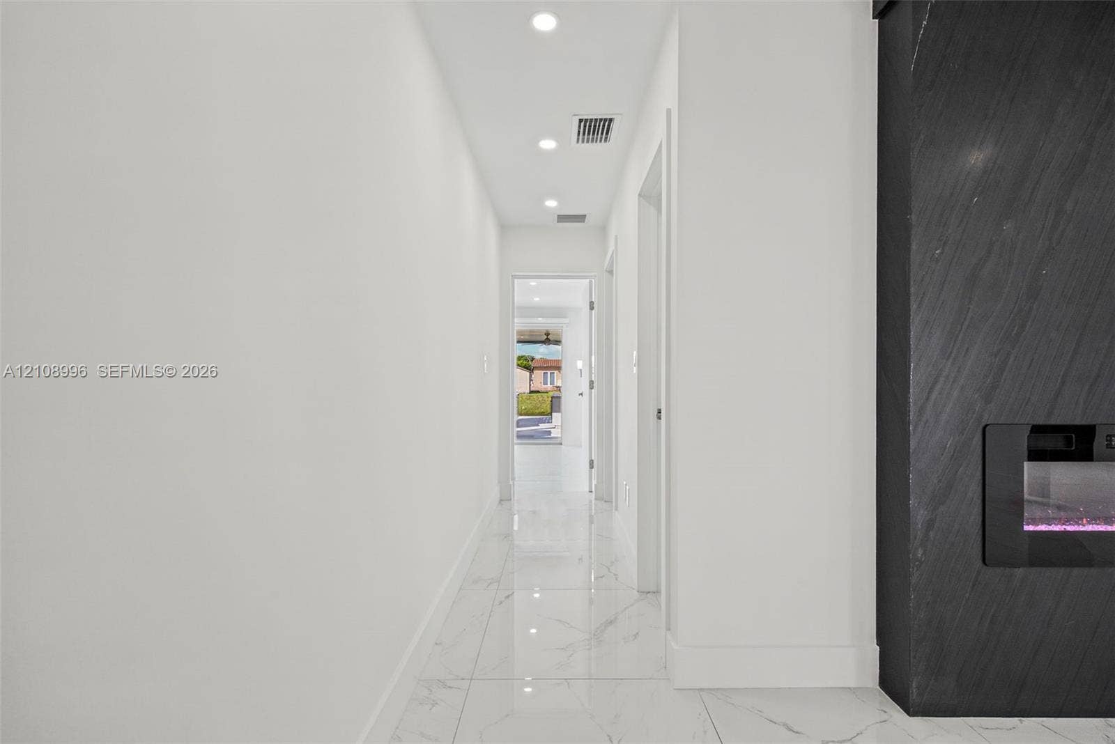 4252 SW 131st Avenue, Miami, FL 33175 Hallway featuring large-format stone-look porcelain tile flooring, recessed ceiling lighting, and a floor-to-ceiling charcoal-toned stone fireplace surround with a built-in linear electric insert
