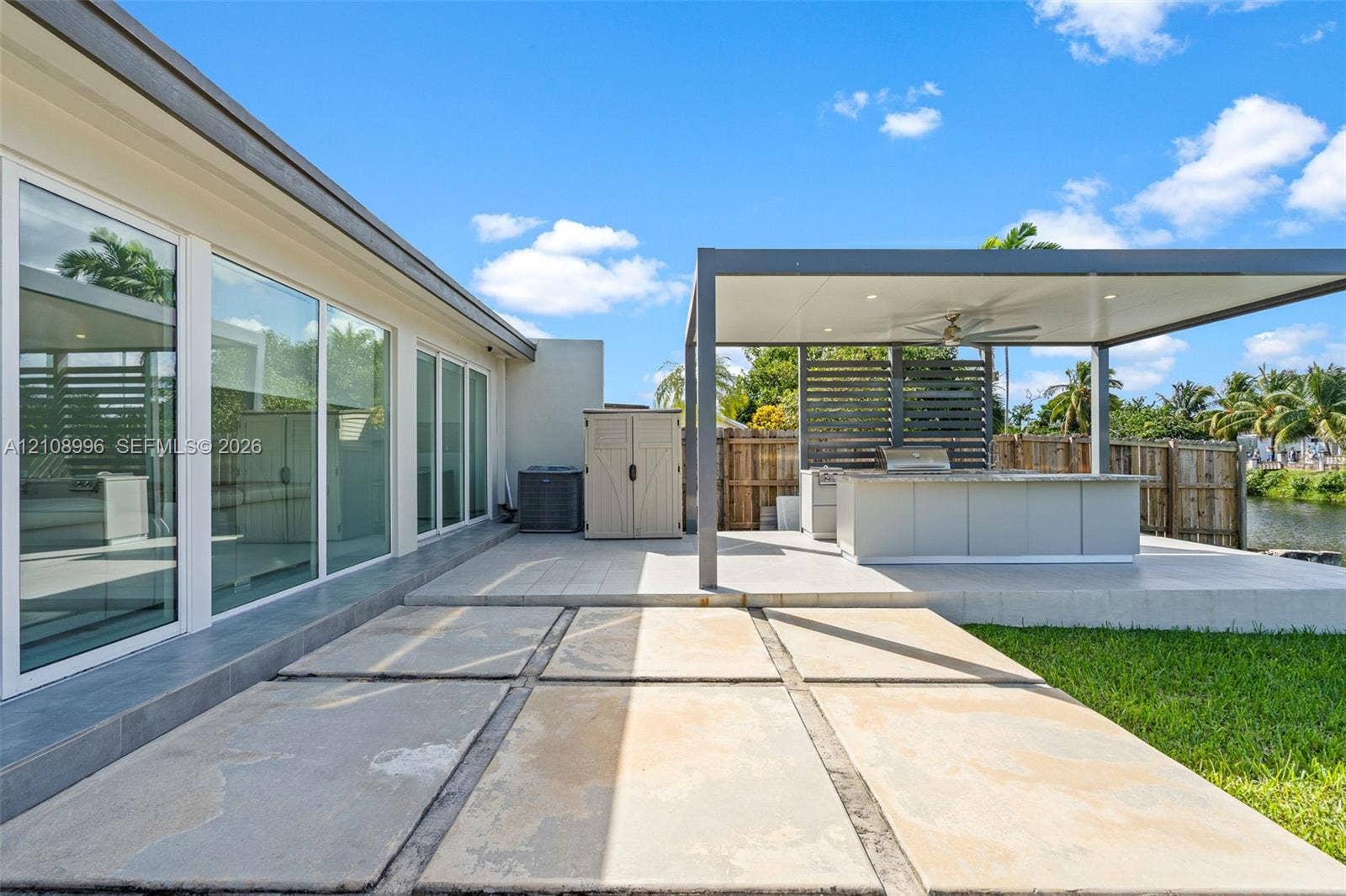 4252 SW 131st Avenue, Miami, FL 33175 Outdoor patio featuring large-format concrete pavers, a covered pergola with recessed lighting and ceiling fan, a built-in outdoor kitchen with countertop, and floor-to-ceiling glass panels