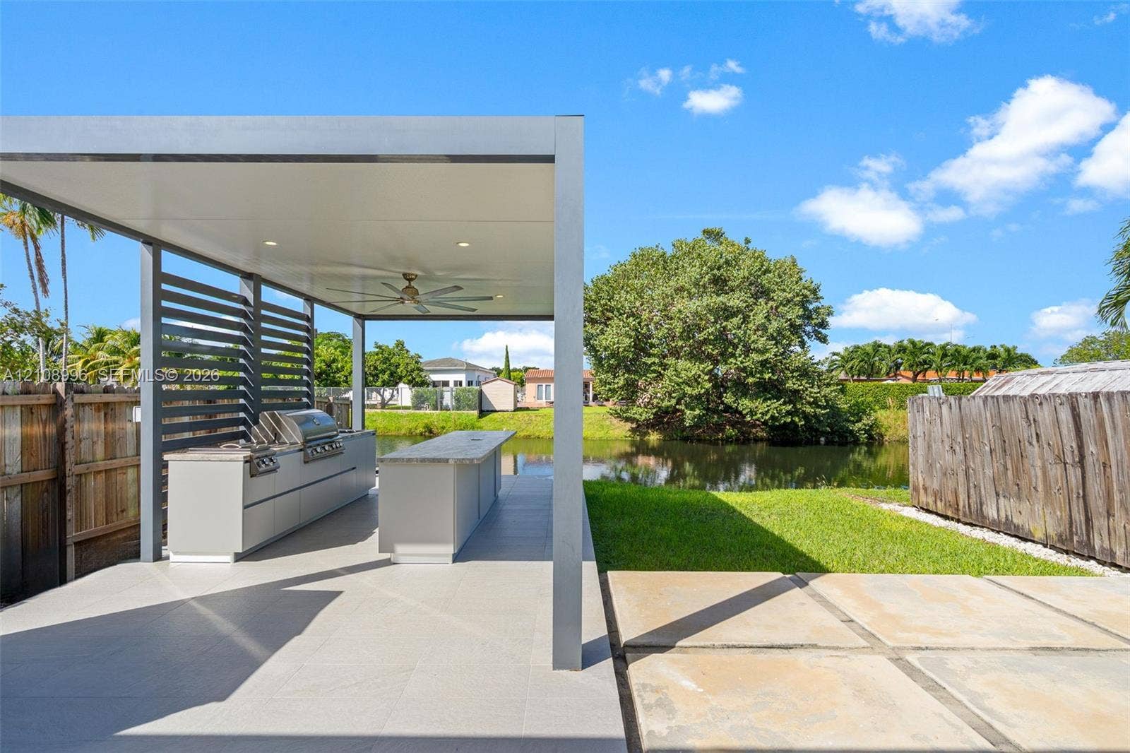 4252 SW 131st Avenue, Miami, FL 33175 Outdoor kitchen featuring a built-in stainless steel grill, stone-topped island, modern pergola structure with recessed lighting and a ceiling fan, and large-format paved patio flooring