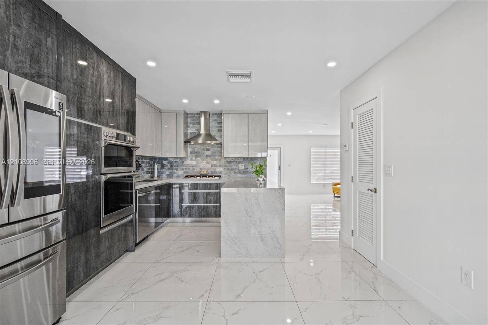 4252 SW 131st Avenue, Miami, FL 33175 Kitchen featuring two-tone cabinetry with high-gloss finishes, a center island with stone-finish waterfall edges, stainless steel built-in appliances, a glass tile backsplash, and large-format porcelain tile flooring