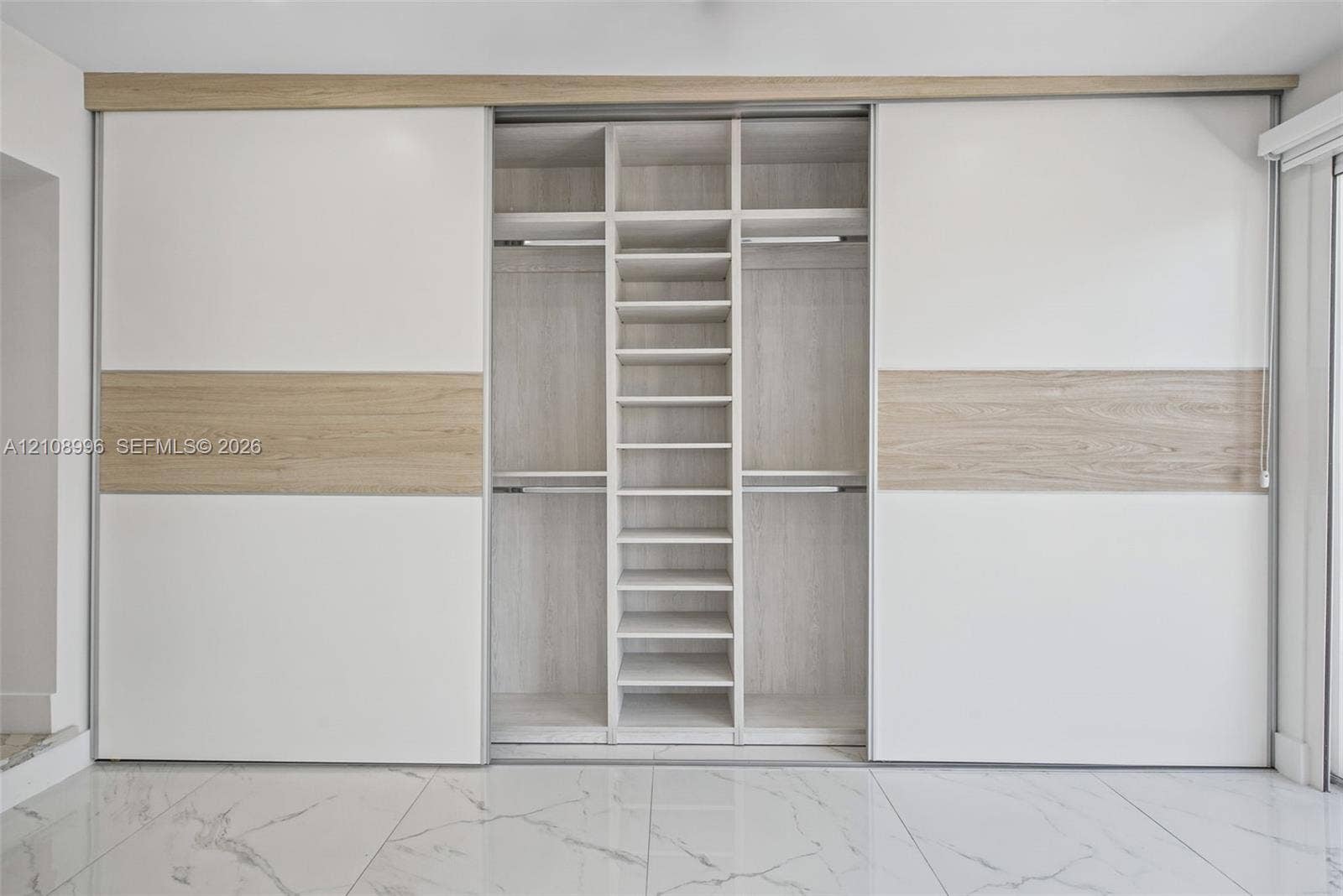 4252 SW 131st Avenue, Miami, FL 33175 Built-in floor-to-ceiling wardrobe featuring sliding dual-tone panel doors, integrated shelving, hanging rods, and light wood-finish interior detailing, complemented by large-format polished tile flooring