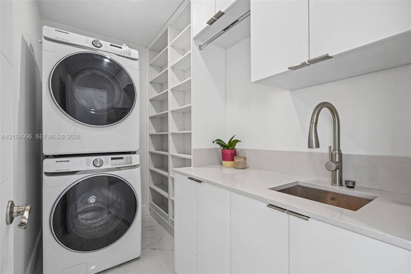 4252 SW 131st Avenue, Miami, FL 33175 Laundry area featuring custom white cabinetry, stone-surface countertop with an integrated basin, high-arc pull-down faucet, floor-to-ceiling built-in shelving, and large-format tile flooring