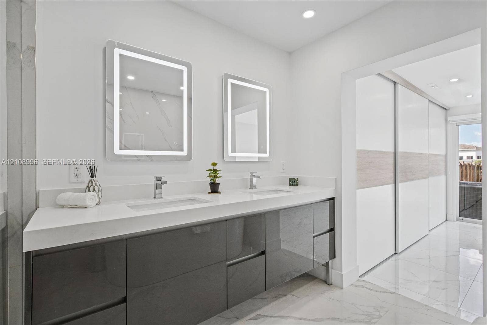 4252 SW 131st Avenue, Miami, FL 33175 Dual-sink vanity featuring high-gloss charcoal cabinetry, white quartz countertop, integrated LED-backlit mirrors, and large-format tile flooring